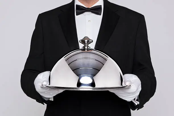 Waiter serving a meal under a silver cloche or dome
