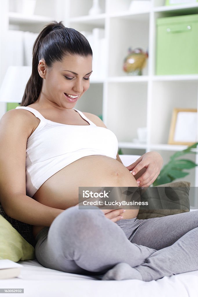 Sonriente mujer embarazada mirando en el vientre - Foto de stock de Abdomen libre de derechos