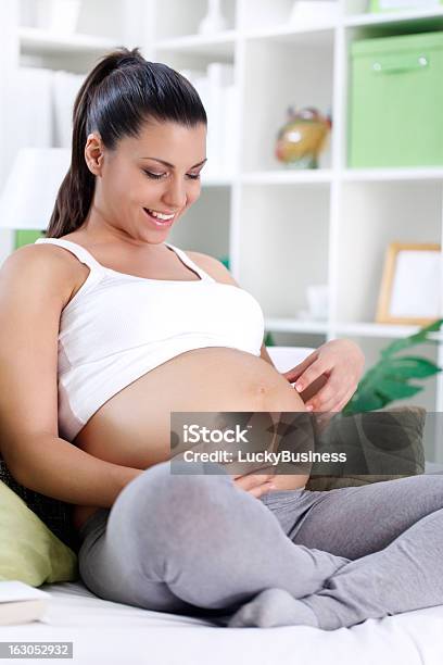 Sonriente Mujer Embarazada Mirando En El Vientre Foto de stock y más banco de imágenes de Abdomen - Abdomen, Abdomen humano, Acogedor