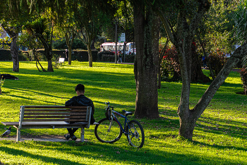 Cuenca, Ecuador - June 6, 2023: Scene of the citylife. A man with a bicycle rests in the green area of the city of Cuenca in the park at sunset