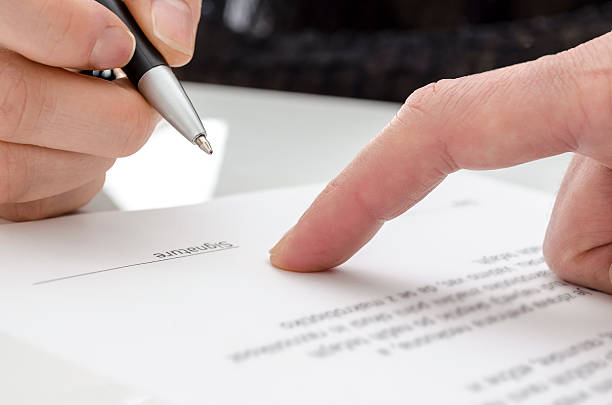 Woman signing a paper Detail of a woman signing a paper. Male finger showing where to sign. witness signature stock pictures, royalty-free photos & images