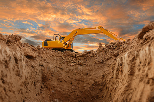 Excavators are digging the soil in the construction site on the orange sky  background of sunset