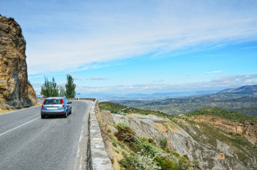 A car is driving on the asphalt road along the mountain slope in the Spanish Sierra Nevada.