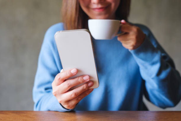 istock Closeup image of a young woman holding and using mobile phone while drinking coffee 1630717289