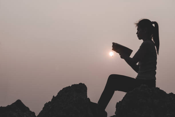 mujeres de pie sosteniendo la santa biblia para adorar a dios en el fondo de la puesta del sol, orar al dios, concepto de silueta cristiana. - god freedom arms raised high angle view fotografías e imágenes de stock