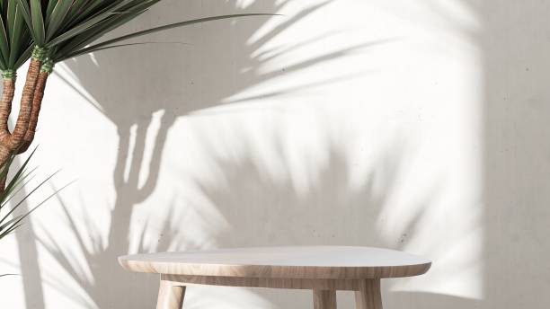istock Wooden triangle pedestal side table podium, tropical dracaena tree in sunlight, leaf shadow on white cement wall 1630737900