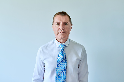 Portrait of confident business mature man 50 years old in white shirt with tie looking at camera on light background