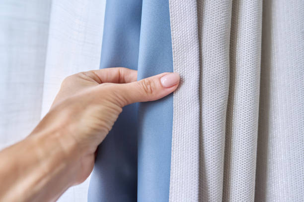 istock Woman's hand showing light gray curtain on blue opaque lining, fabric blackout 1630757562