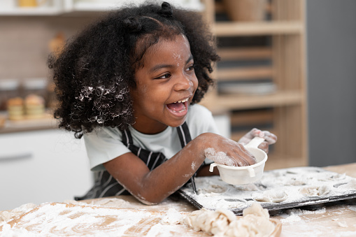 Happy African American kid girl cooking break or bakery at kitchen at home