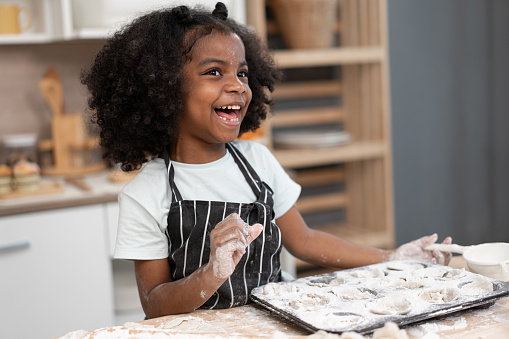 Happy African American kid girl cooking break or bakery at kitchen at home