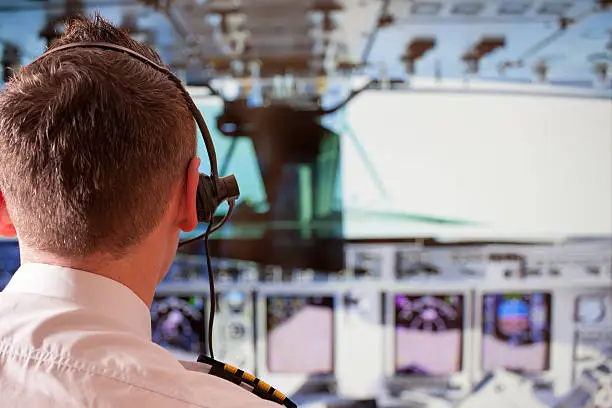 Airline pilot wearing uniform with epaulettes and headset working in airliner during flight.
