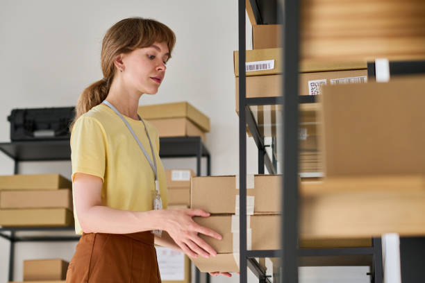 istock Young woman in yellow blouse putting boxes on rack in warehouse 1630842864