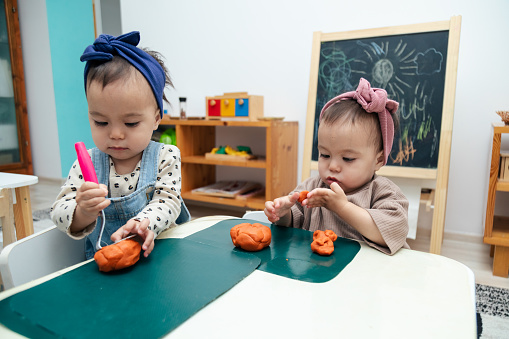 Toddlers playing with colorful modeling clay or Play-Doh on a table in the kindergarten