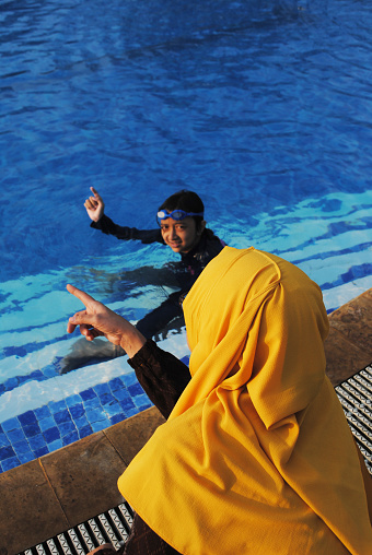 Indonesian hijab mother and daughter are having conversation in the side of swimming pool.