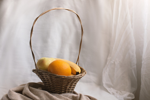Still life composition of fruit in a wicker basket in a soft, cozy space. Healthy nutrition concept.