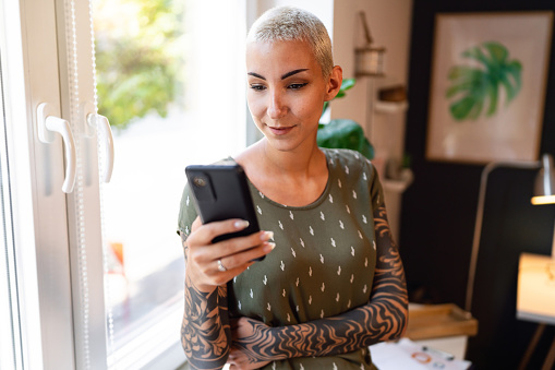 Young Caucasian woman with short blond hair and sleeve tattoo, using mobile phone