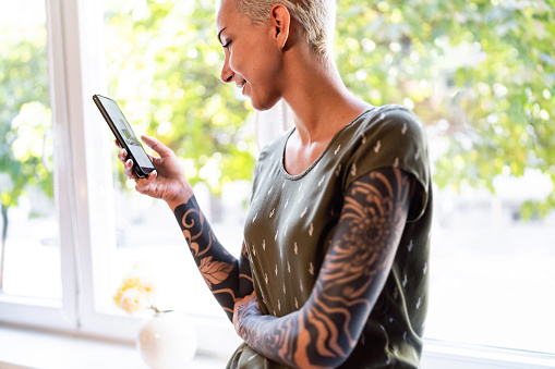 Young Caucasian woman with short blond hair and sleeve tattoo, using mobile phone