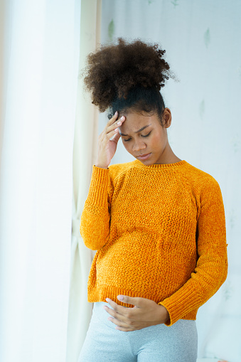 Happy cheerful African - American black pregnant woman standing near the window in bedroom and enjoy looking a natural view outside close up with copyspace. Pregnant woman portrait.