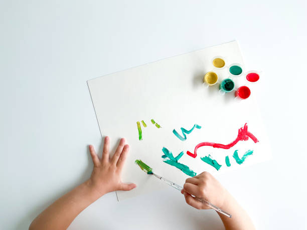 istock small child draws with paints and brush on white table. 1630991650