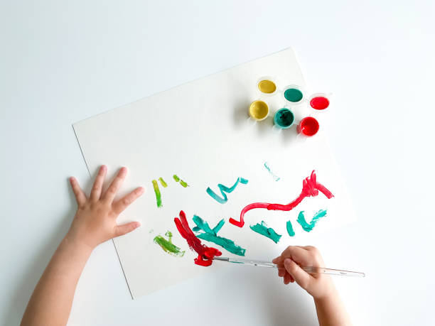 istock small child draws with paints and brush on white table. 1630991653