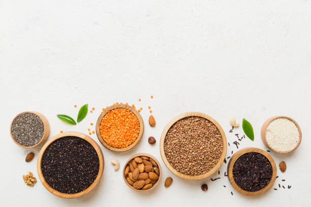 varios superalimentos en tazón pequeño sobre fondo de color. superalimentos como arroz, chía, quinoa, lentejas, nueces, semillas de sésamo, almendras. espacio de copia de vista superior - quinoa sesame chia flax seed fotografías e imágenes de stock