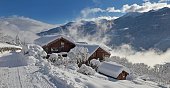 chalets in alpine village covered with snow at the end of a white rural road and mountain background