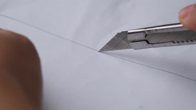 Hands cutting paper with stainless steel cutter. Paper cutting with paper knife close up.