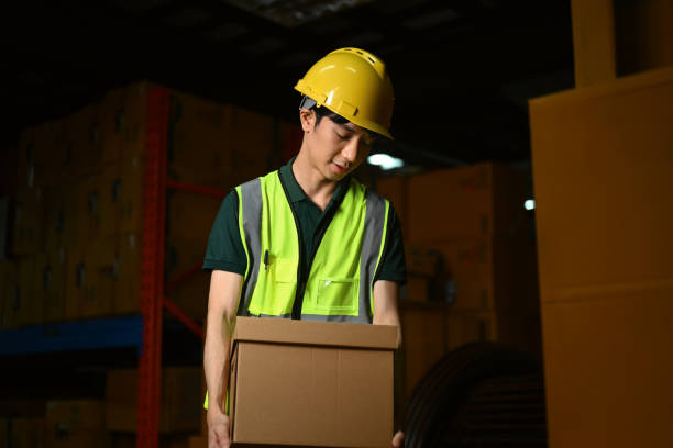 istock Warehouse worker holding cardboard box walking through retail warehouse full of packed boxes and goods 1631048639