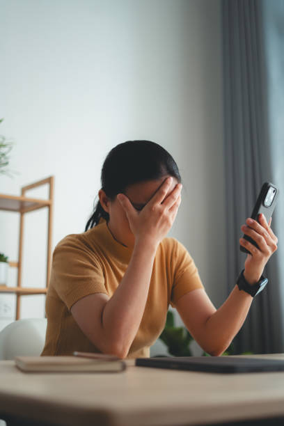 istock Asian woman sitting at home office looking at smartphone screen and having problem. 1631054157