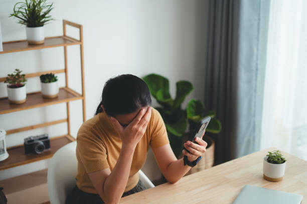 istock Asian woman sitting at home office looking at smartphone screen and having problem. 1631055734