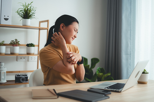 Asian woman suffering from irritate dry skin and scratching her skin sitting at home office.