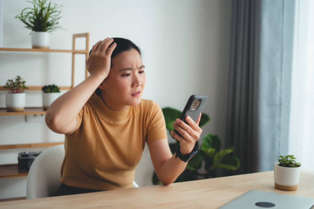 istock Asian woman sitting at home office looking at smartphone screen and having problem. 1631057915