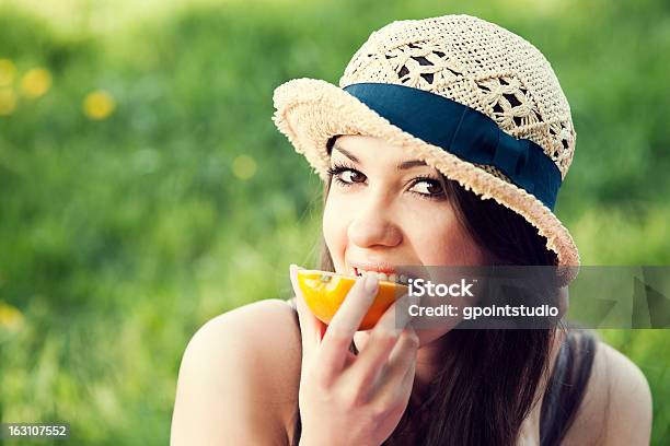 Schöne Frau Essen Orange Auf Wiese Stockfoto und mehr Bilder von Attraktive Frau - Attraktive Frau, Beißen, Blick in die Kamera