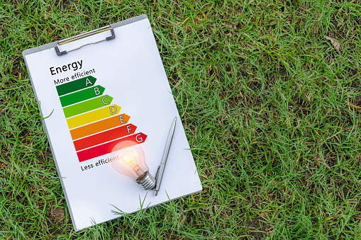 A light bulb is placed on a piece of paper that indicates the energy efficiency rating of an appliance indicating how much electricity it should save.laying on the green lawn