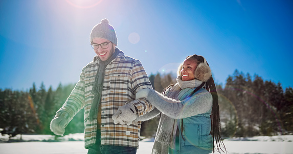 Smiling young couple holding hands while ice skating on frozen lake in winter.