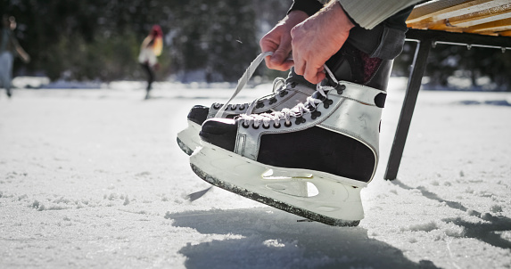 Man's hands tying shoelaces of ice skates on frozen lake in winter.