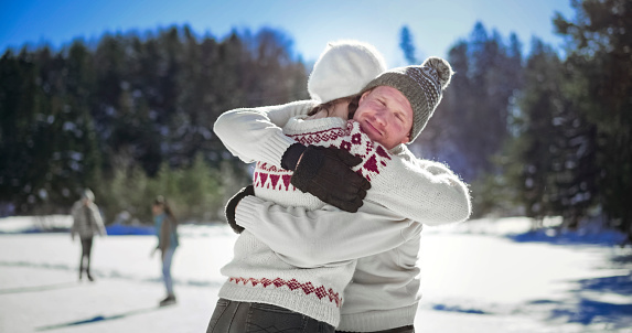 Couple embracing each other while standing on frozen lake during ice skating.