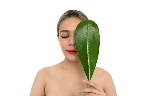 Young asian woman playfully covering her face with a vibrant green leaf. Portrait on white background. Facial treatment,  beauty, Cosmetology