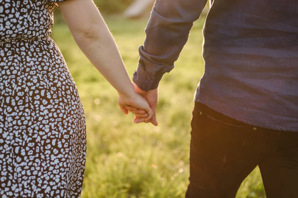 Couple hands. Man holds hands woman. Young couple walk back at sunset outdoors. Man and woman on field grass on background of sun. full length. Portrait of romantic male and female in love on nature. manos de pareja. el hombre toma de la mano a la mujer. pareja joven camina de regreso al atardecer al aire libre. hombre y mujer en el césped del campo sobre el fondo del sol. longitud total. retrato de hombre y mujer románticos enamorados de la naturale