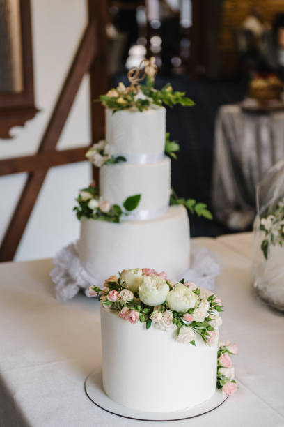 istock Wedding white cake decorated pink flowers for a banquet. Selective focus. Delicious reception for luxury wedding ceremony. Trendy cake. Closeup. Stylish cake for newlyweds on a table in restaurant. 1631095576