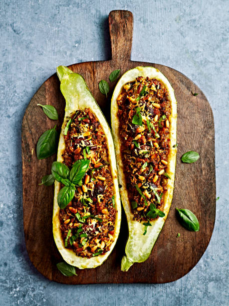 Oven baked zucchinis stuffed with minced meat, bulgur and vegetables; topped with olives, pine nuts and parmesan stock photo