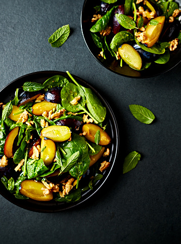 Autumnal plum and spinach salad with toasted walnuts, honey and mint leaves. Top view. Black background