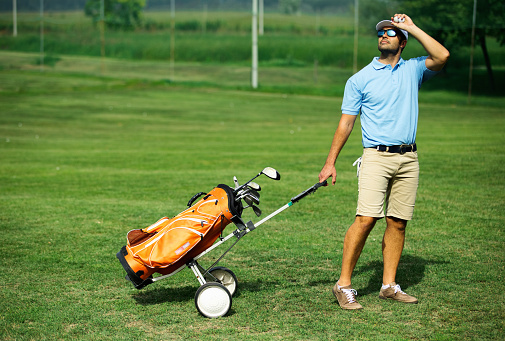 Closeup front view of a young man walking to the driving range at a golf course and checking the Sun