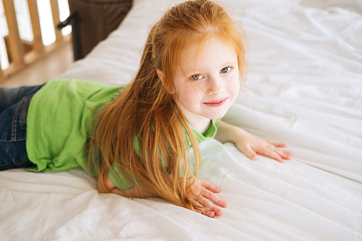 Close up portrait of blonde caucasian little girl looks up at camera  smiles. Childhood, outdoor leisure, vacations. Preschooler girl with braid enjoying nature at country house.