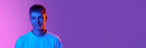 istock Handsome young guy with cute smile looking at camera against gradient pink purple background in neon light 1631159349