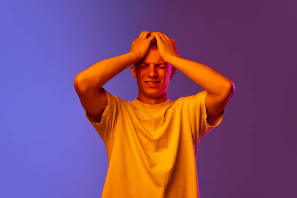 istock Young guy holding hands on head, suffering from stress and deadlines against gradient purple background in neon light 1631159373