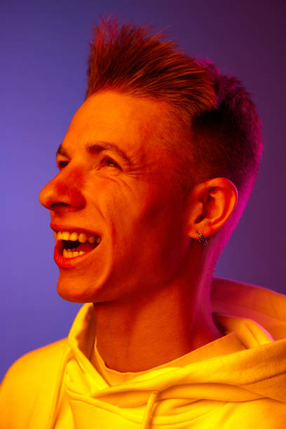 istock Wind blowing on face. Young guy in white hoodie posing against gradient purple background in neon light 1631159911