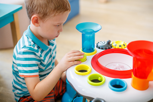 Preschool boy focusing and playing with educational toy at occupational therapy session, learning and developmental difficulties