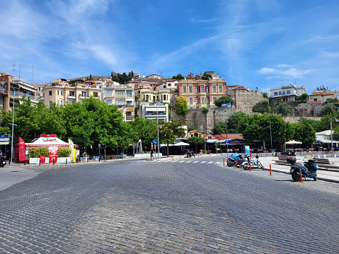 Kavala, Greece - June 12, 2306: Promenade along the port overlooking the colorful buildings in Panagia district on hill with medieval castle above