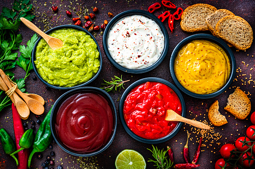 Set of five dip sauces shot from above on dark table. The composition includes guacamole, mayonnaise, Dijon mustard, hot sauce and barbeque sauce. High resolution 42Mp studio digital capture taken with Sony A7rII and Sony FE 90mm f2.8 macro G OSS lens